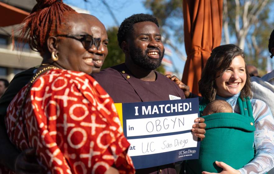A family with a newborn smiles holding a sign that says I Matched! OB/GYN at UC San Diego at the campus' Match Day