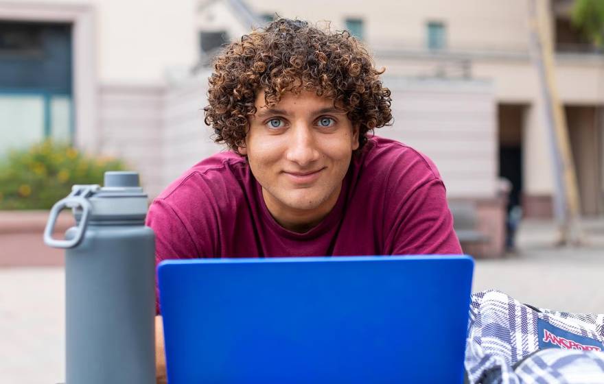A young man with curly hair stares intently above a laptop while sitting outdoors