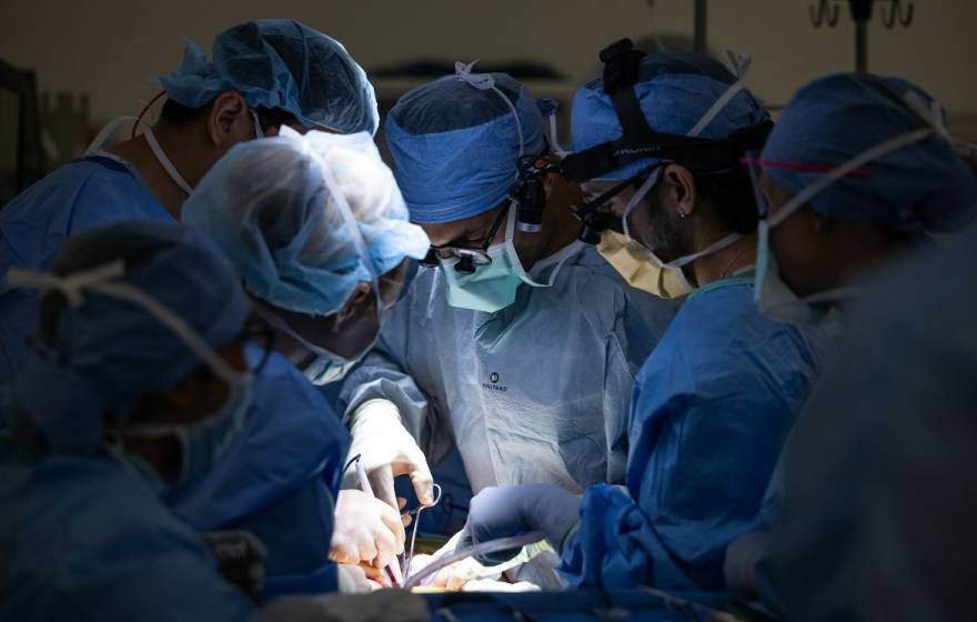 Six surgeons huddle around someone while operating