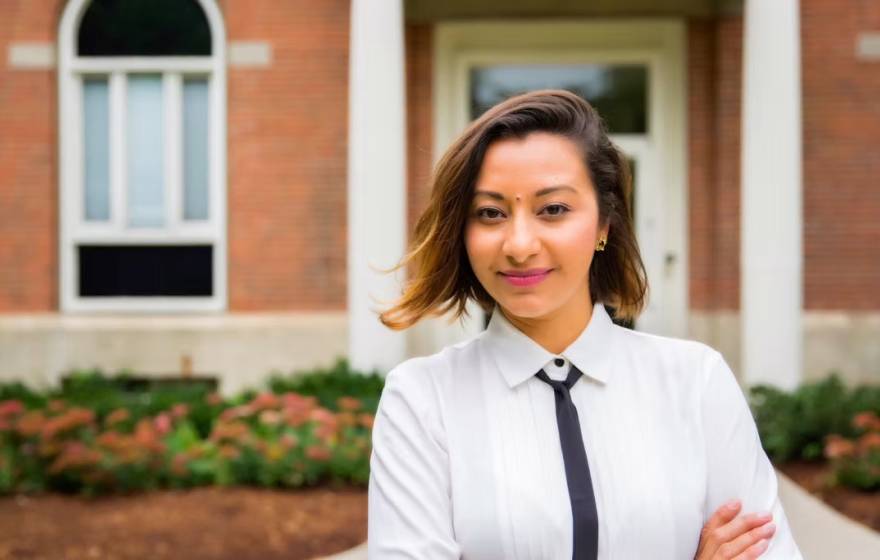 A woman with a skinny tie and arms crossed smiles at camera
