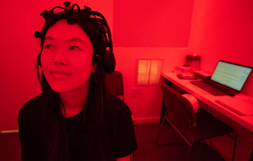 A woman wearing a device on her head sits in a lab bathed in deep red light