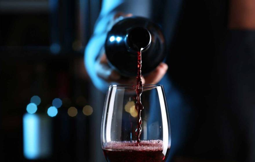 A hand pours a bottle of red wine into a wine glass, centered