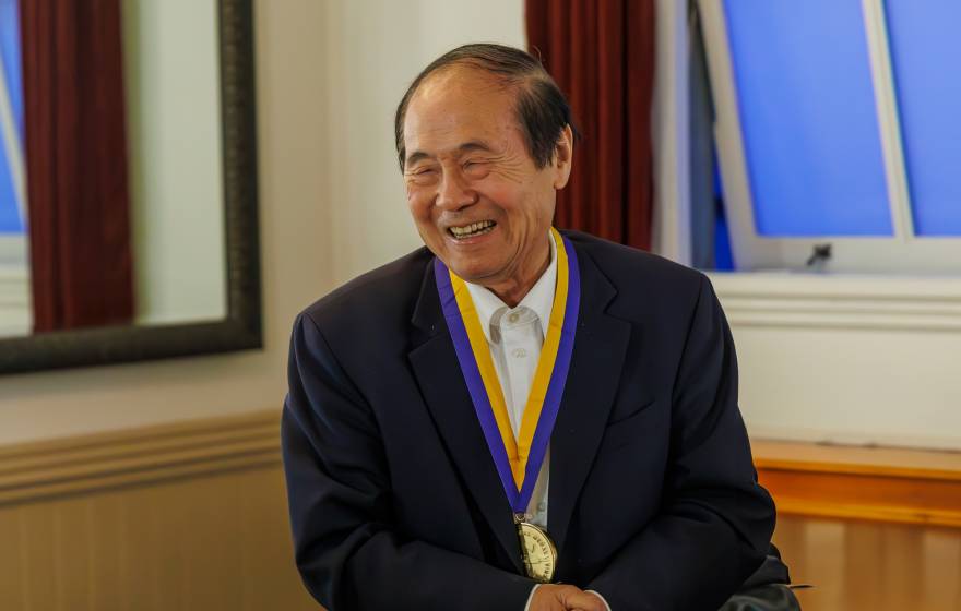 Chancellor Henry T. Yang smiles widely with his hands clasped as he wears his UC Presidential medal