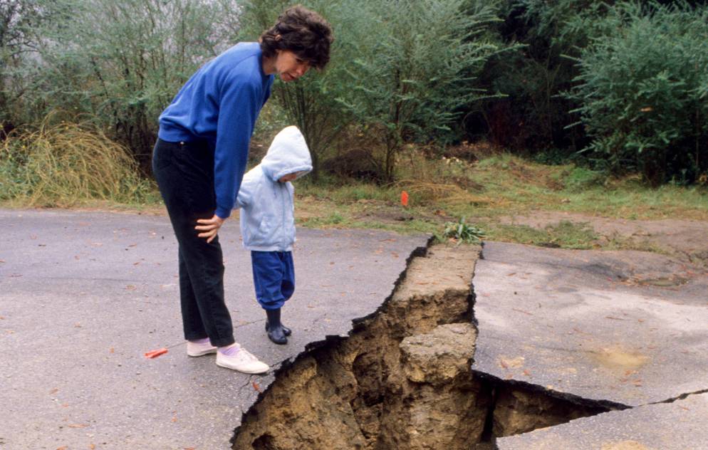 A woman and child look into a large crack in the ground caused by an earthquake.