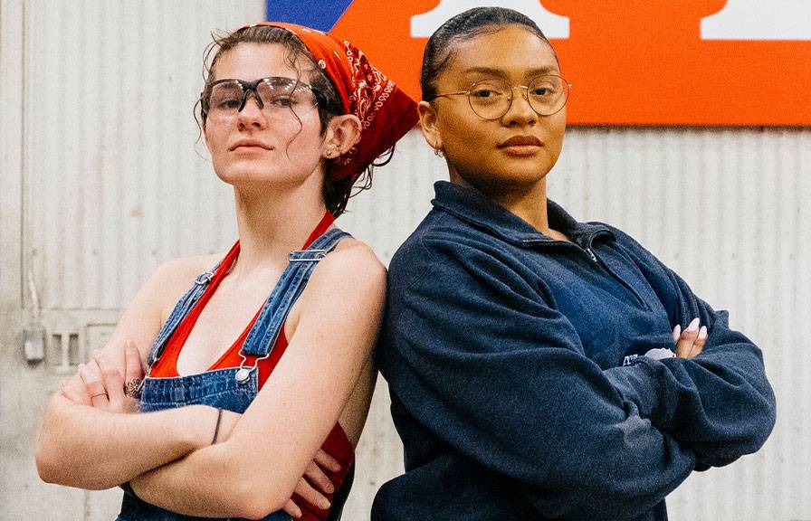 Two students standing back to back with their arms crossed