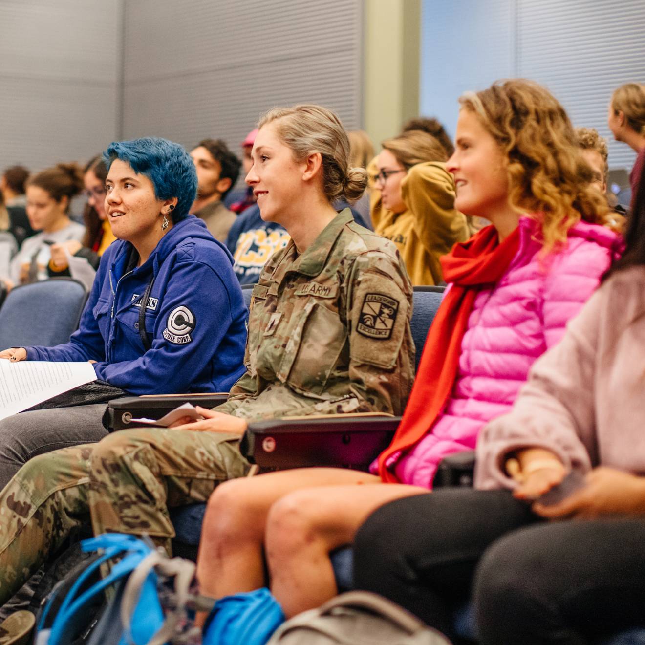 A woman in a U.S. Army uniform sitting in a lecture hall full of students