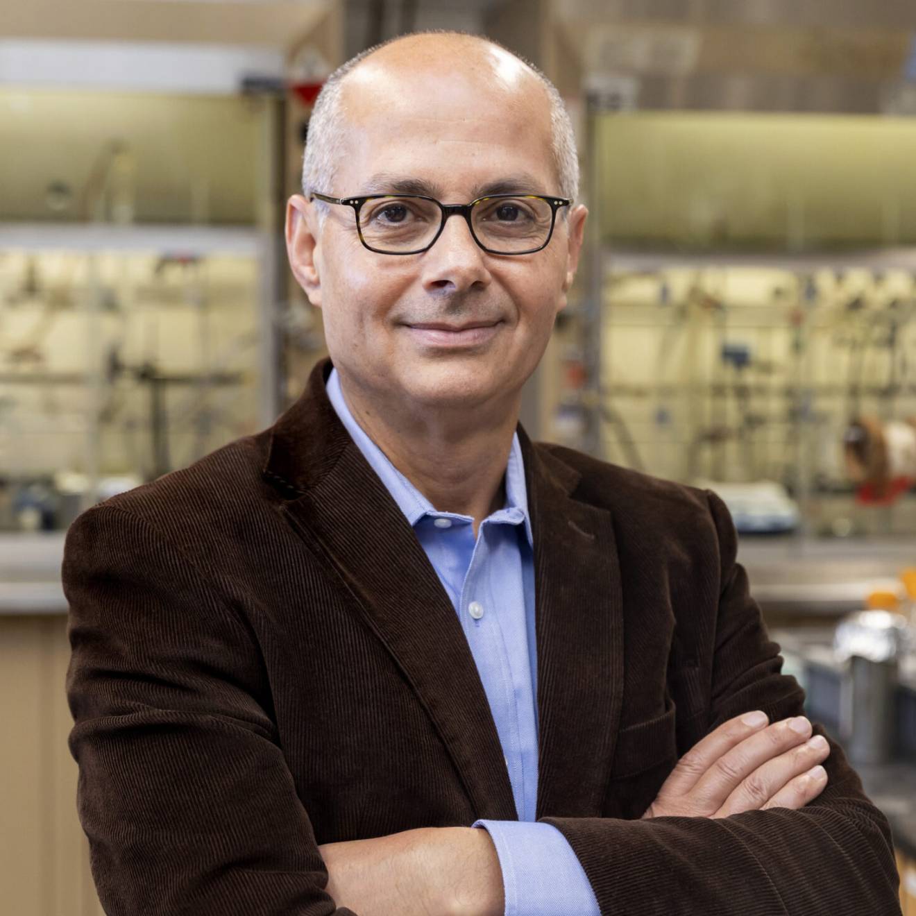 A man with glasses in a brown jacket smiles at the camera in a lab (Omar Yaghi)