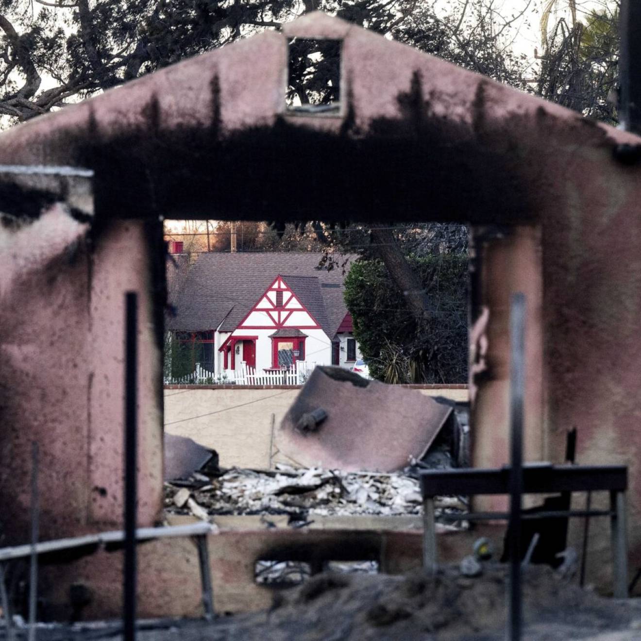 A home destroyed by the Eaton Fire stands in front of a home that survived in Altadena.