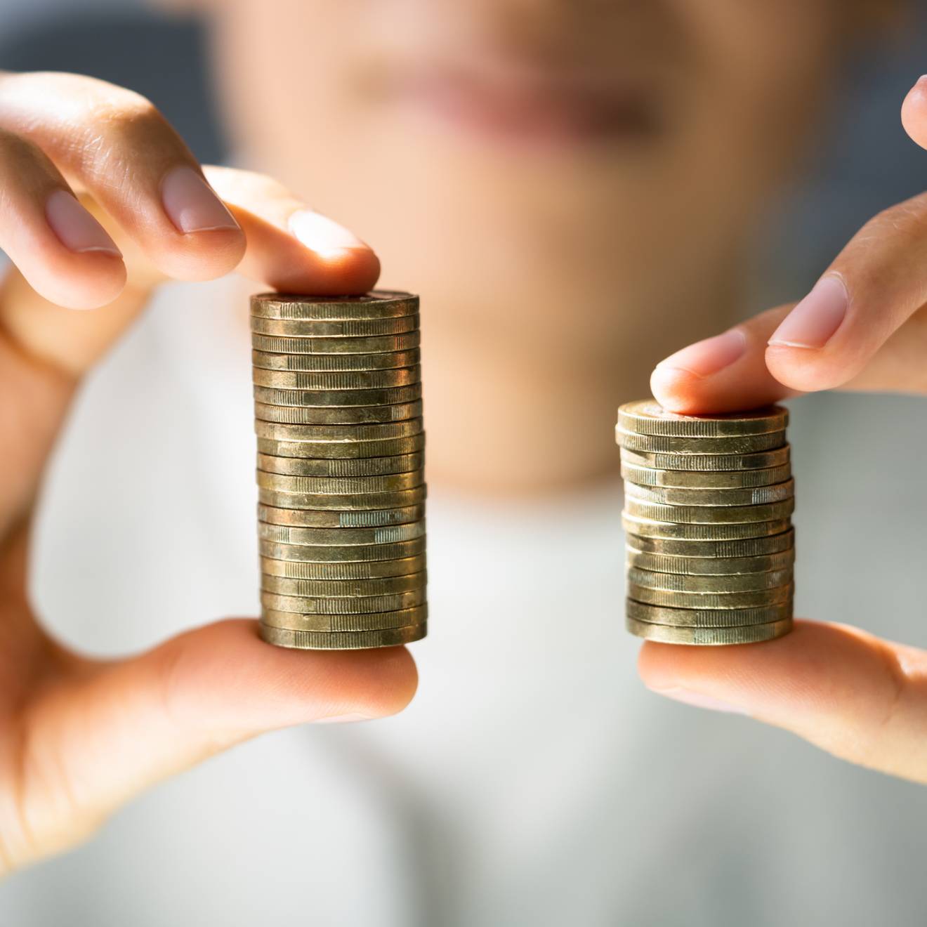 Close up of hands holding two stacks of coins, one larger than the otther
