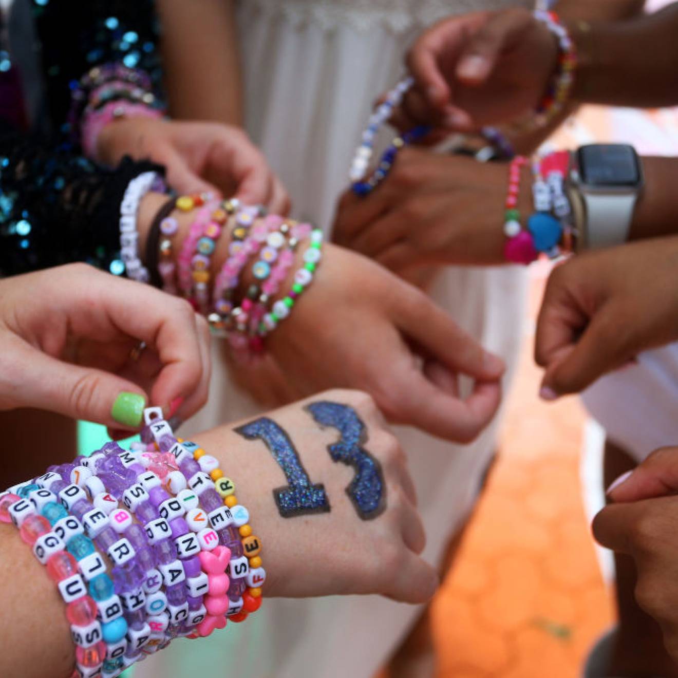 Closeup of the hands of a group of Taylor Swift fans wearing stacks of colorful friendship bracelets