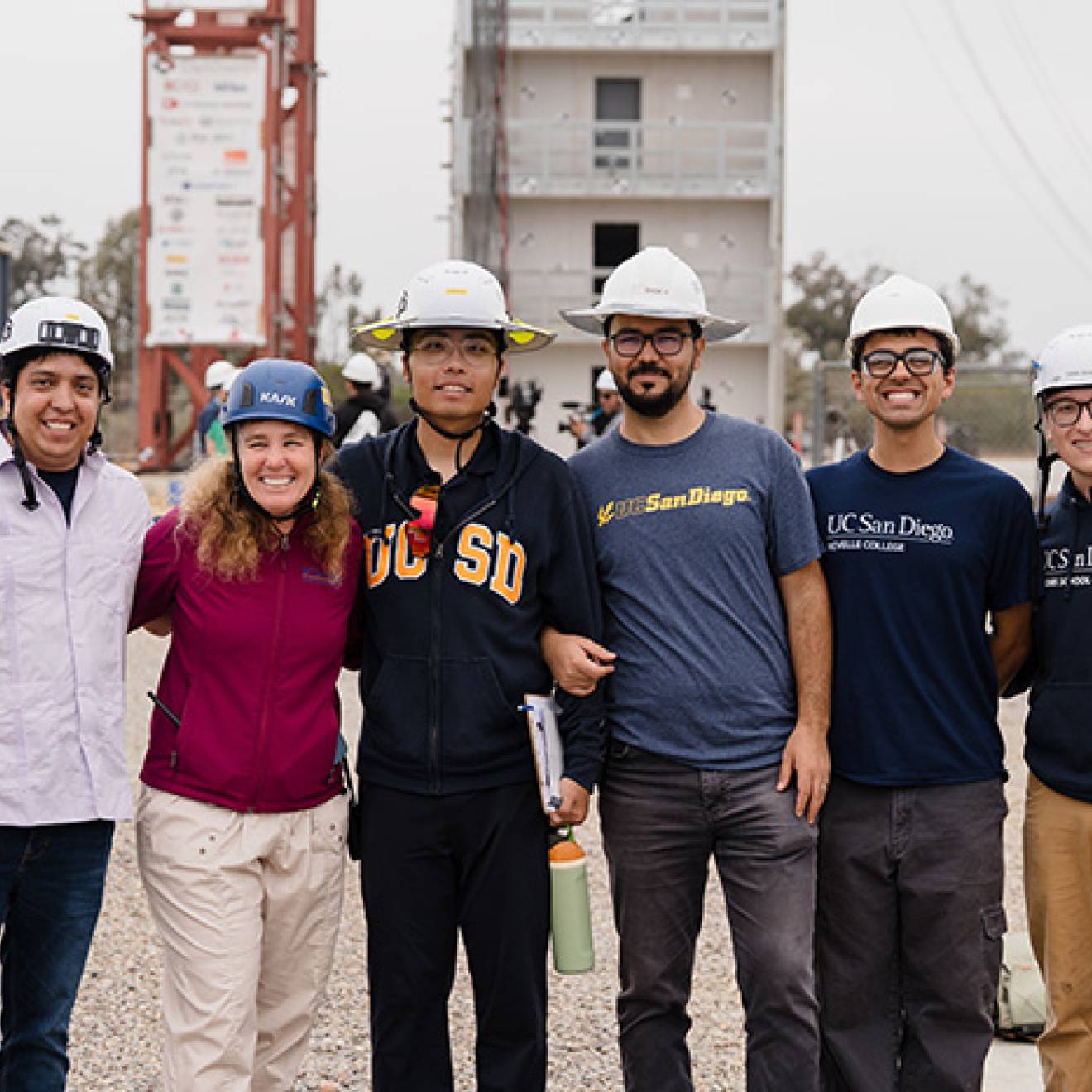 A group of engineers in hard hats stand in front of the earthquake simulator