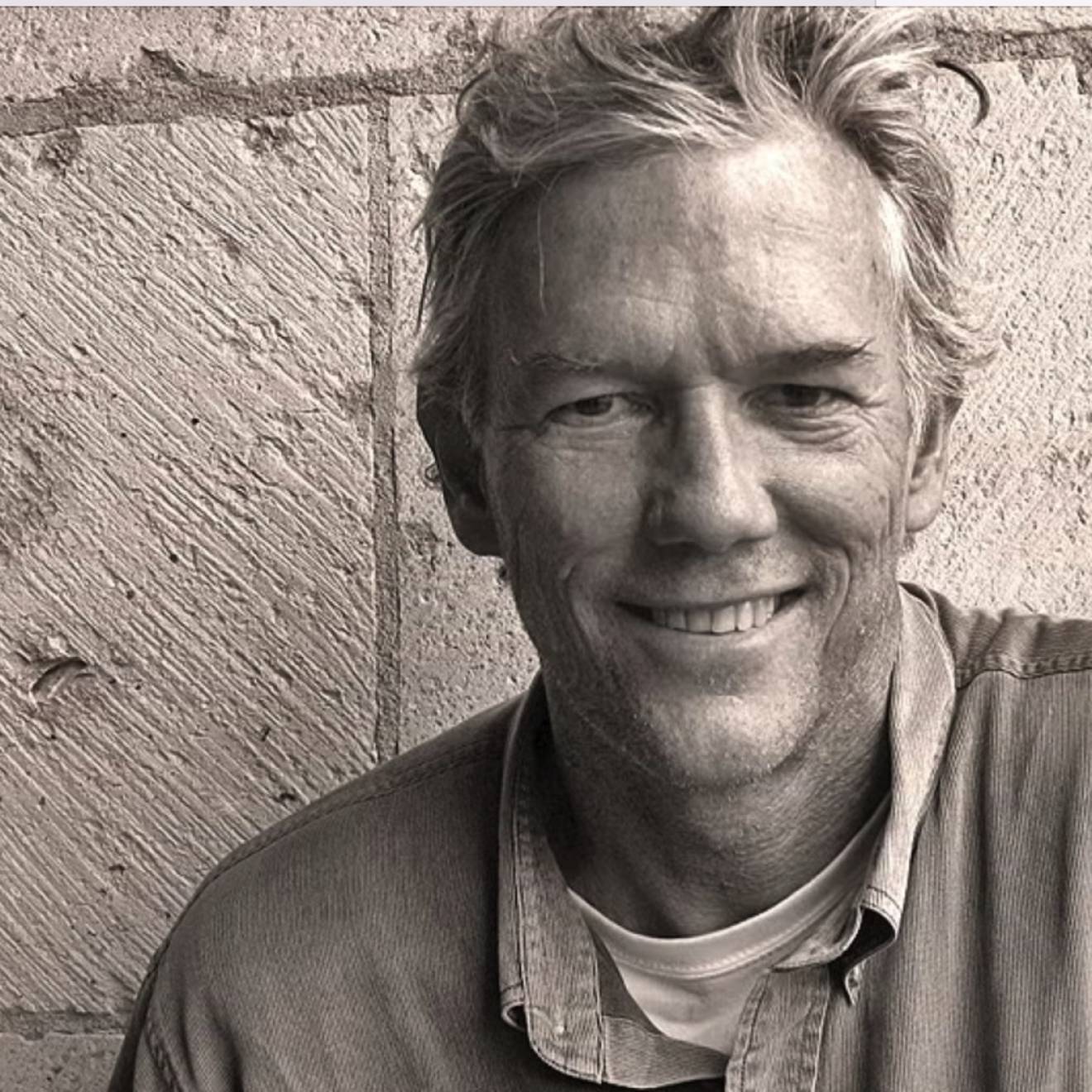 William Finnegan smiles against a brick wall in a sepia-tinted image