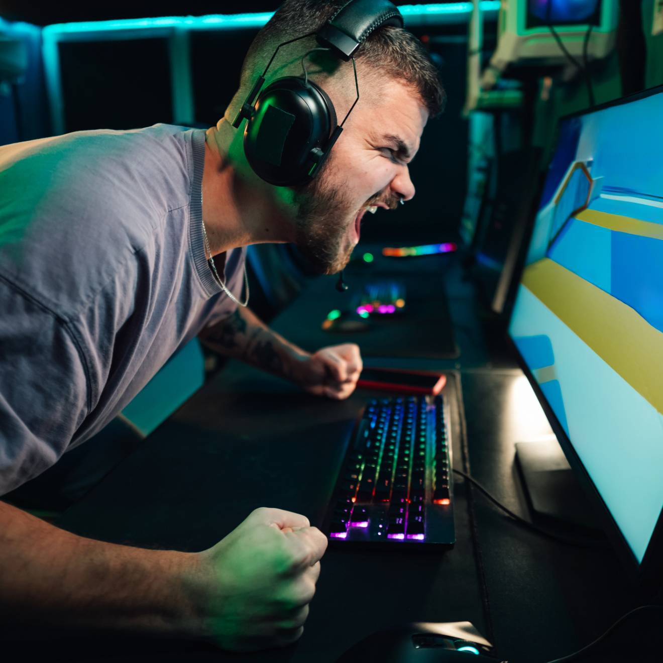 A man wearing headphones and at a keyboard screams at a computer monitor