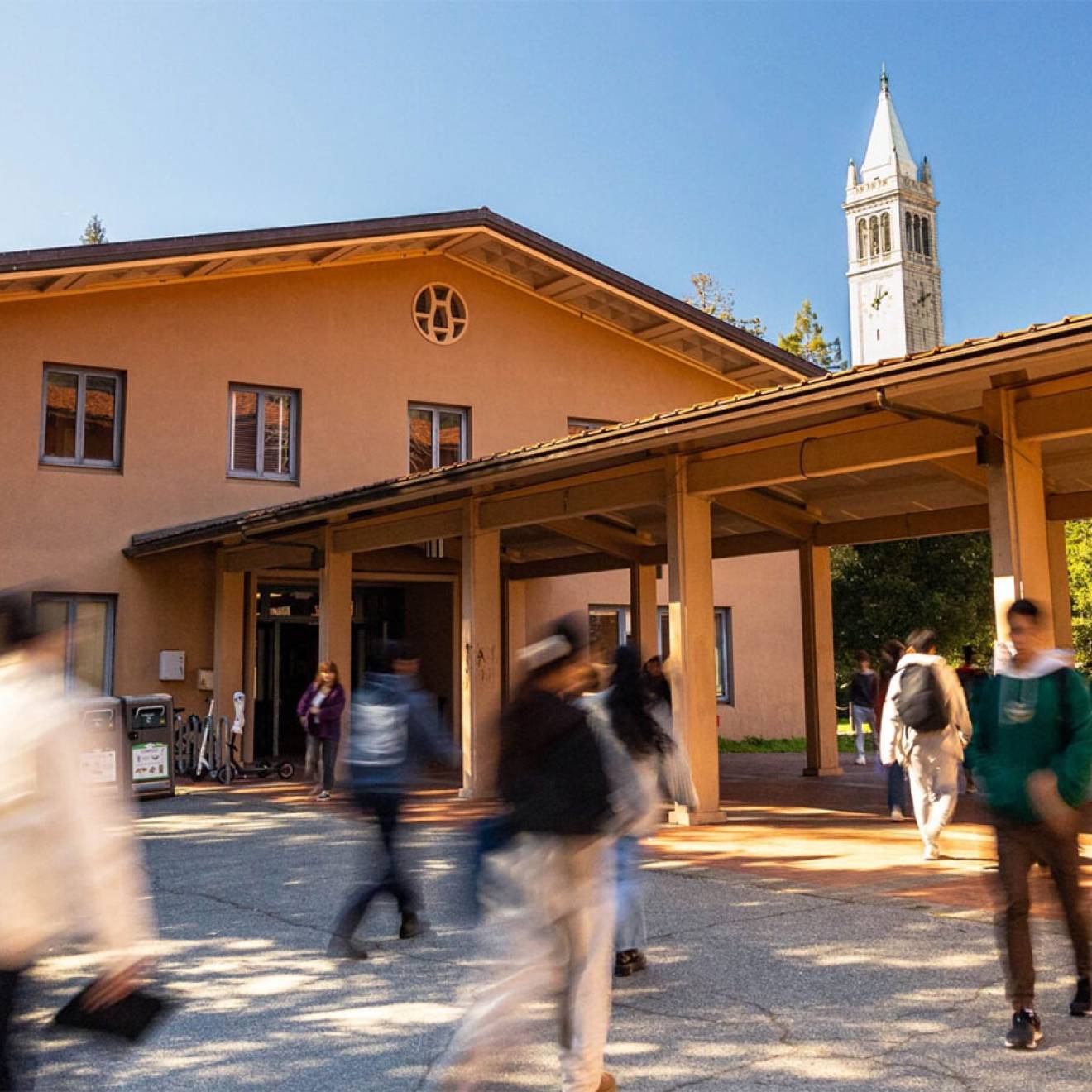 Students walk in front of the music building on Cal's campus, with the campanile in the background