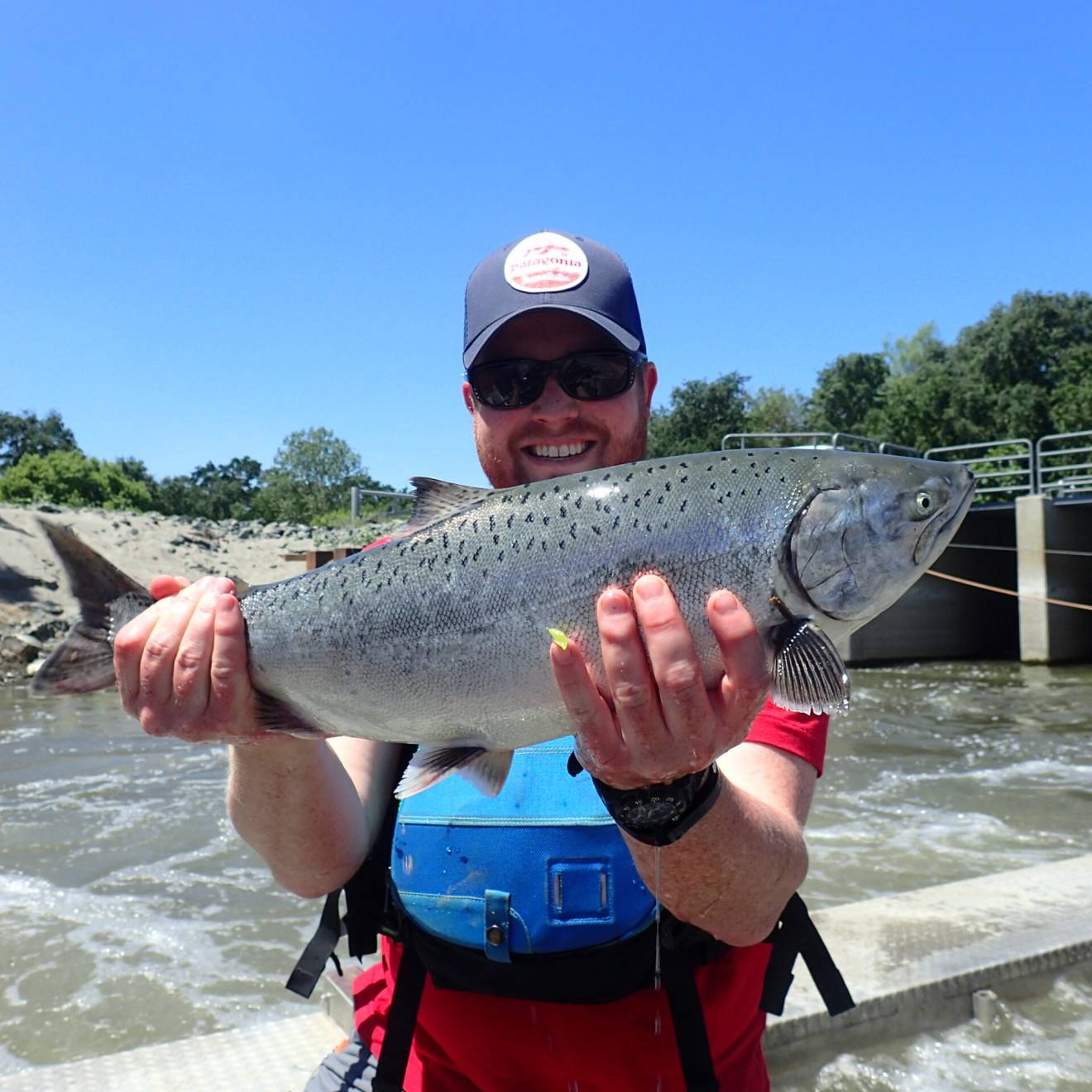 A man holds up a salmon in front of a rushing river