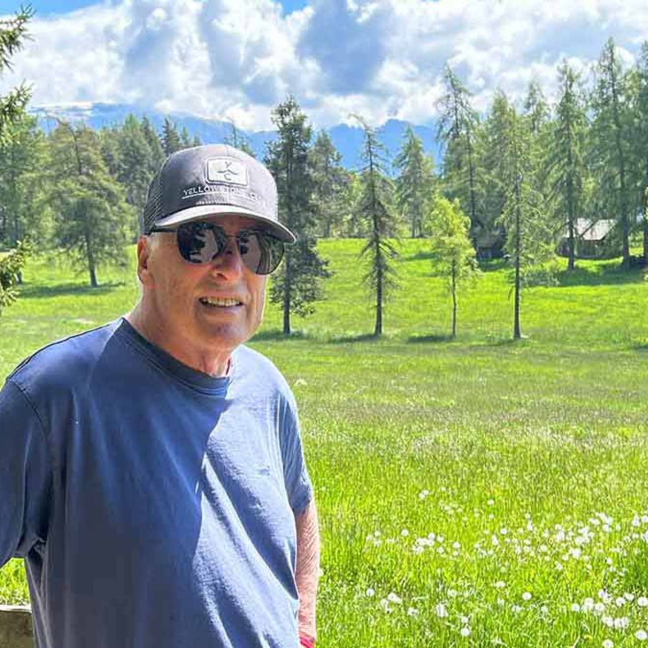A man wearing a ballcap stands in the Sierras on a beautiful day