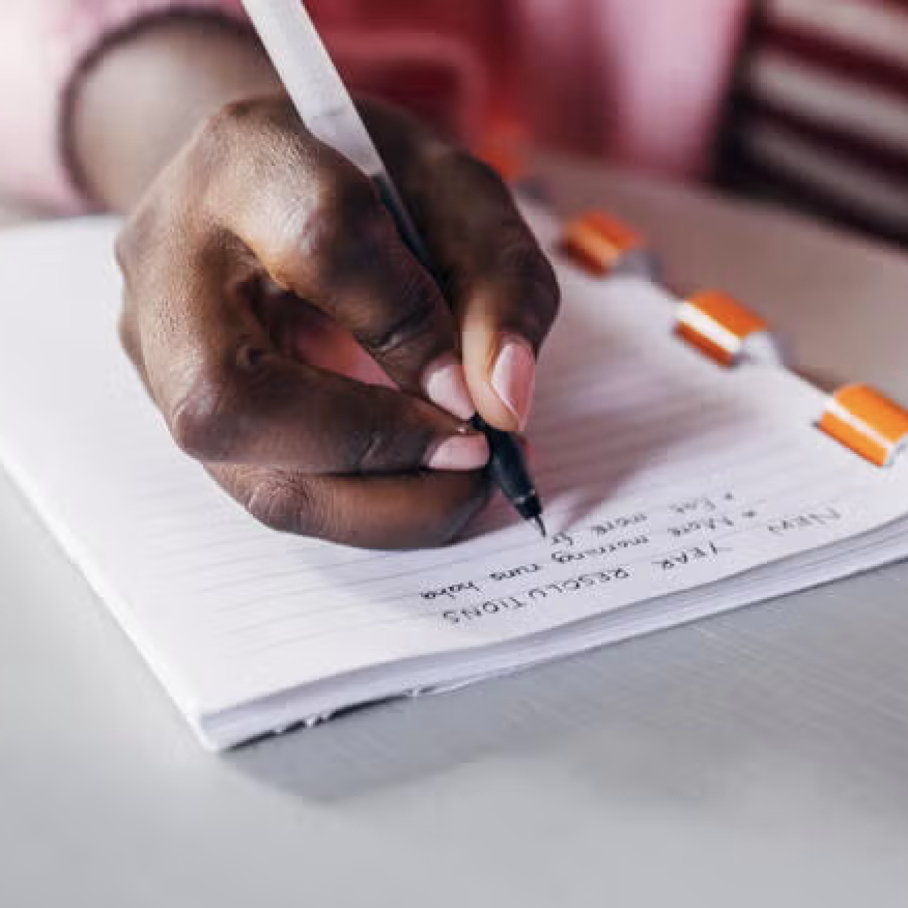 A close-up of a hand holding a pen writing a list in a notebook