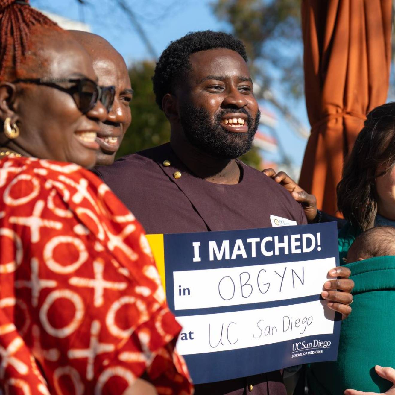 A family with a newborn smiles holding a sign that says I Matched! OB/GYN at UC San Diego at the campus' Match Day