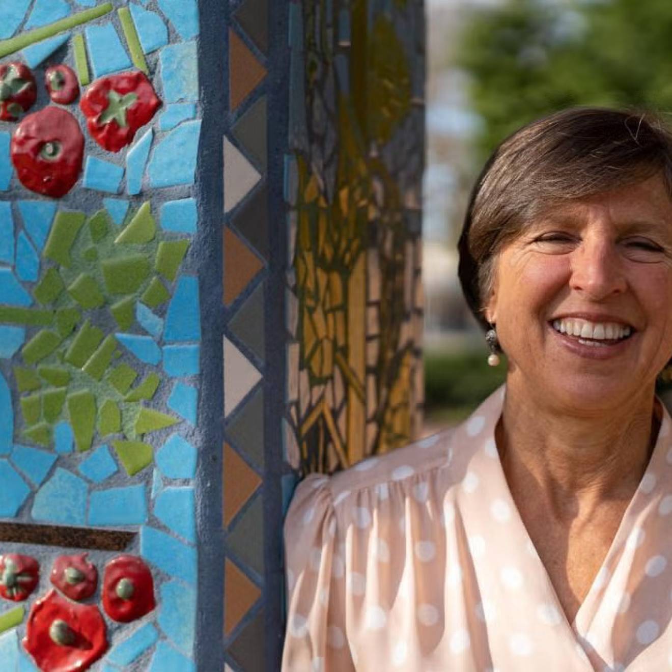 Woman smiles next to an outdoor pillar with a tomato mosaic