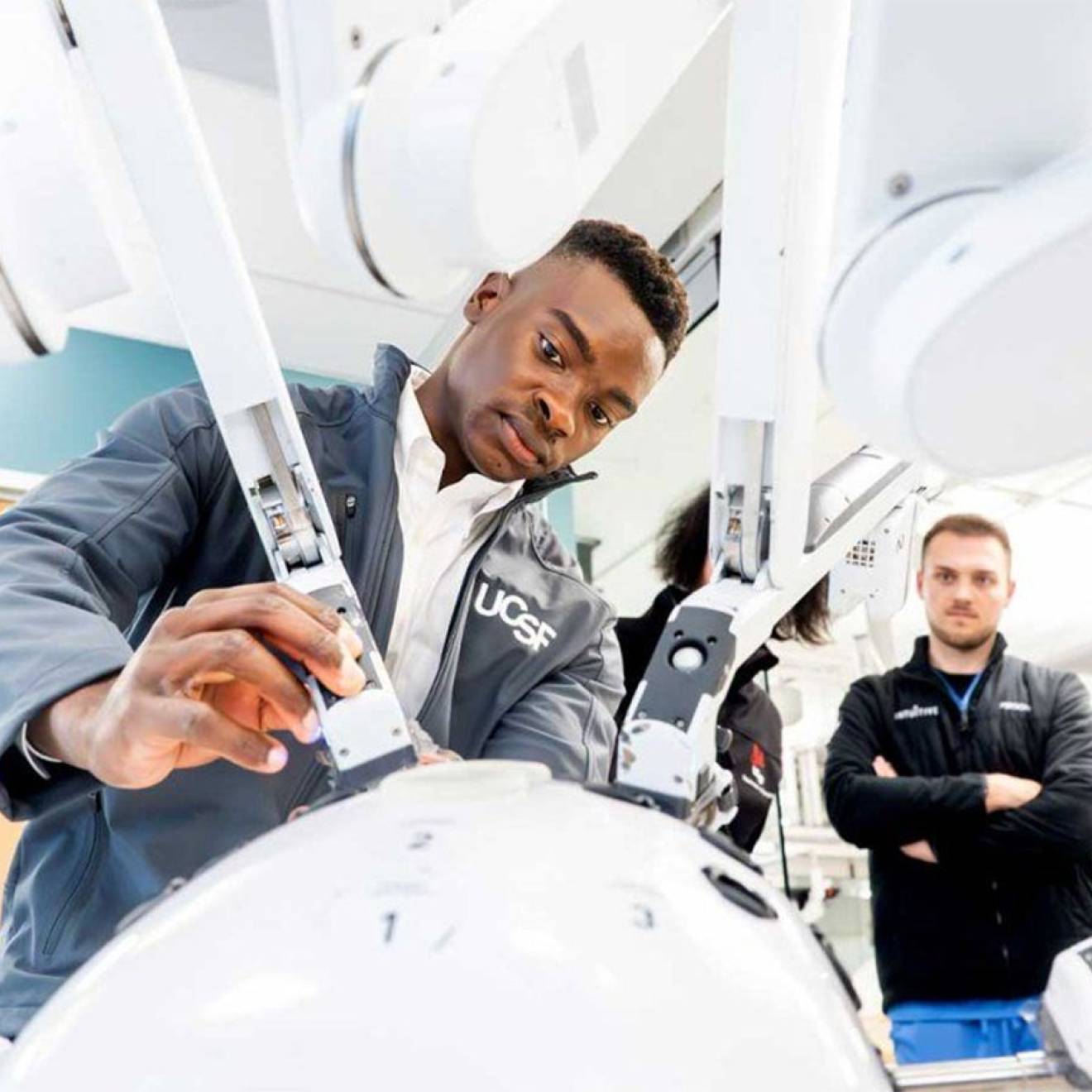 A student focuses intently as he operates one arm of a many-armed robot, while a teacher watches