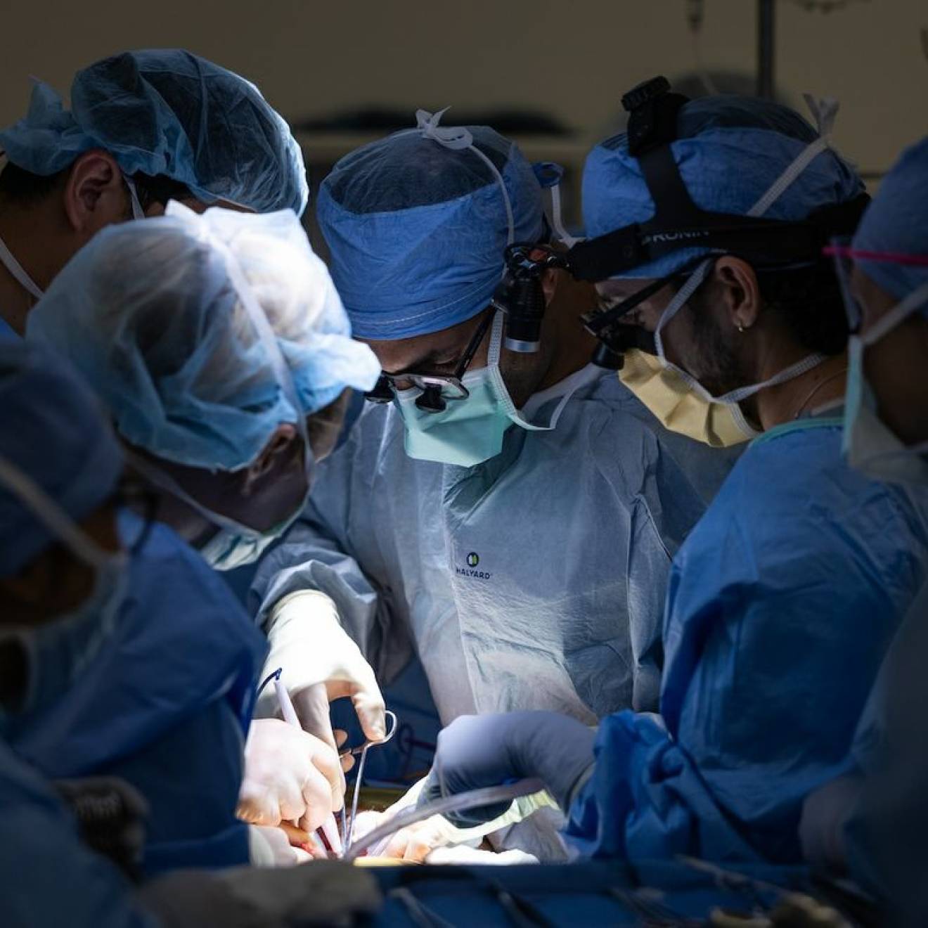 Six surgeons huddle around someone while operating