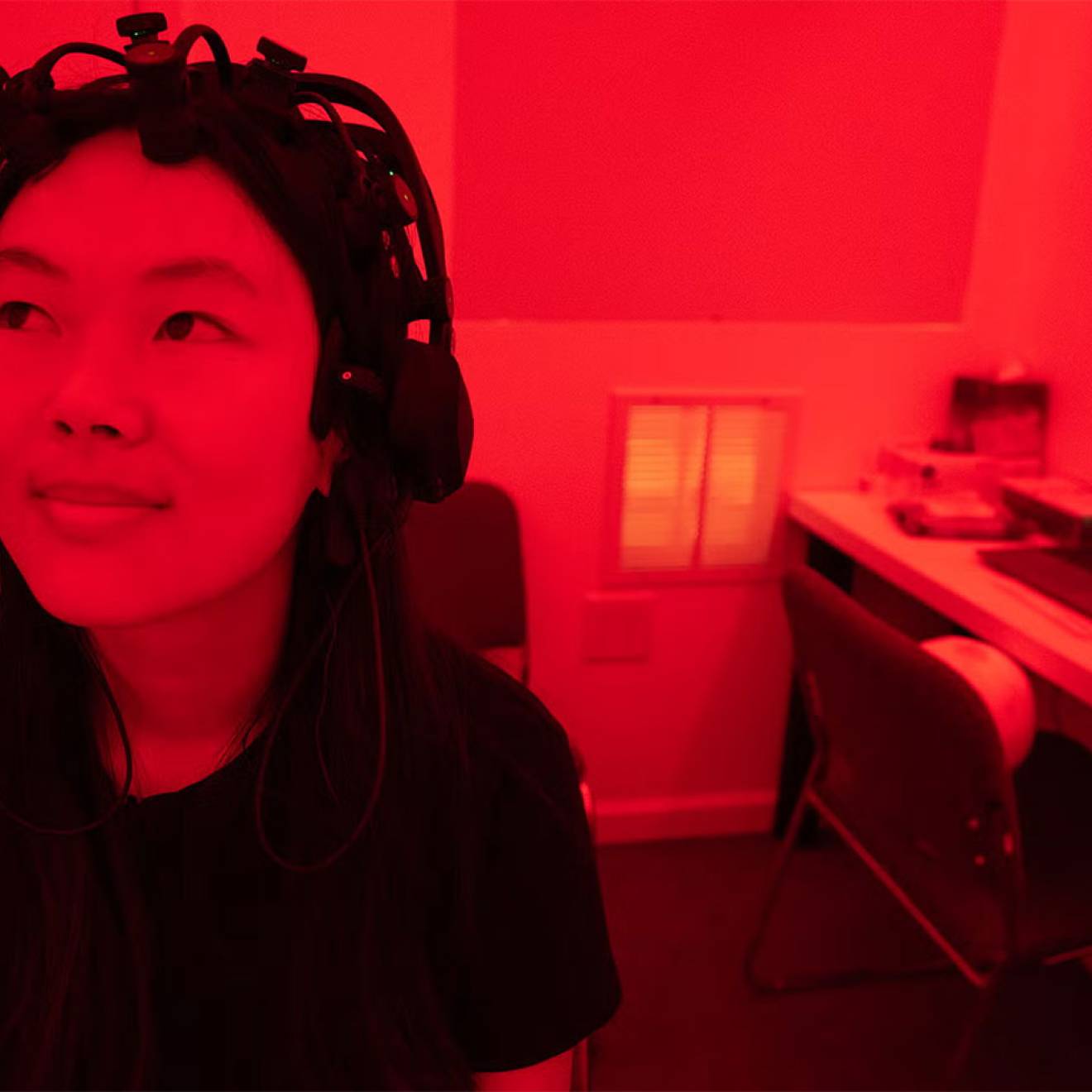A woman wearing a device on her head sits in a lab bathed in deep red light