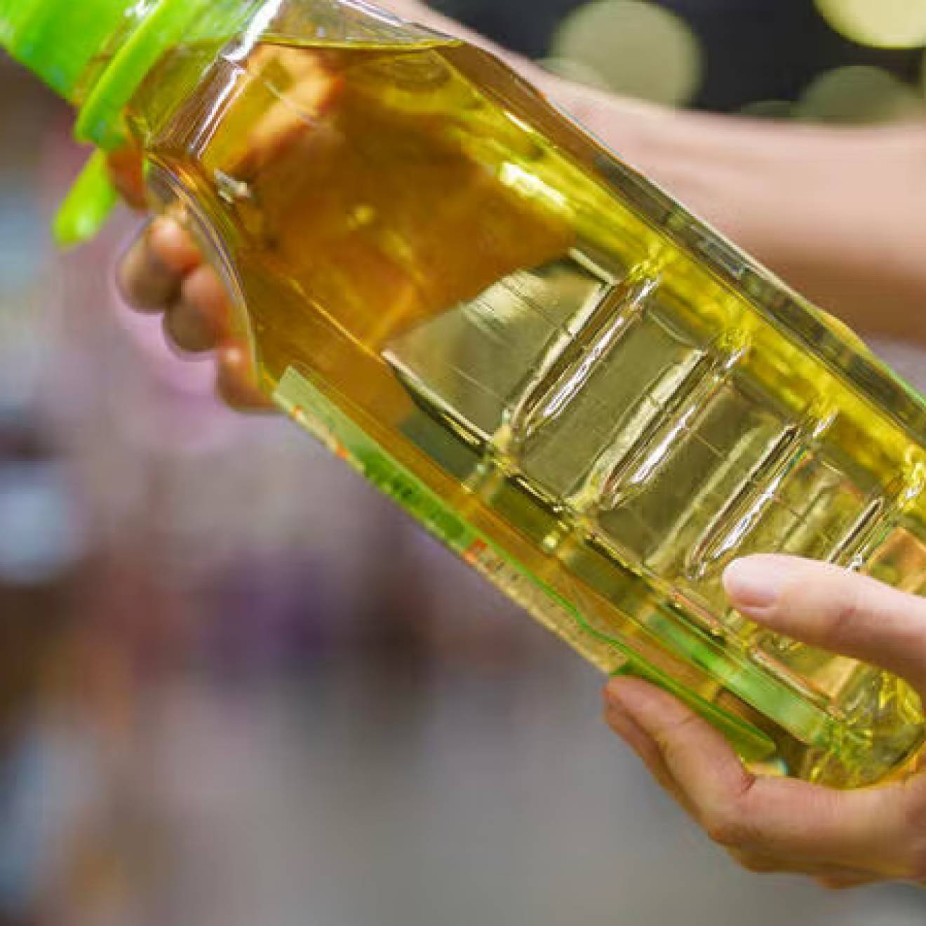 A pair of hands hold a bottle of soybean oil at an angle