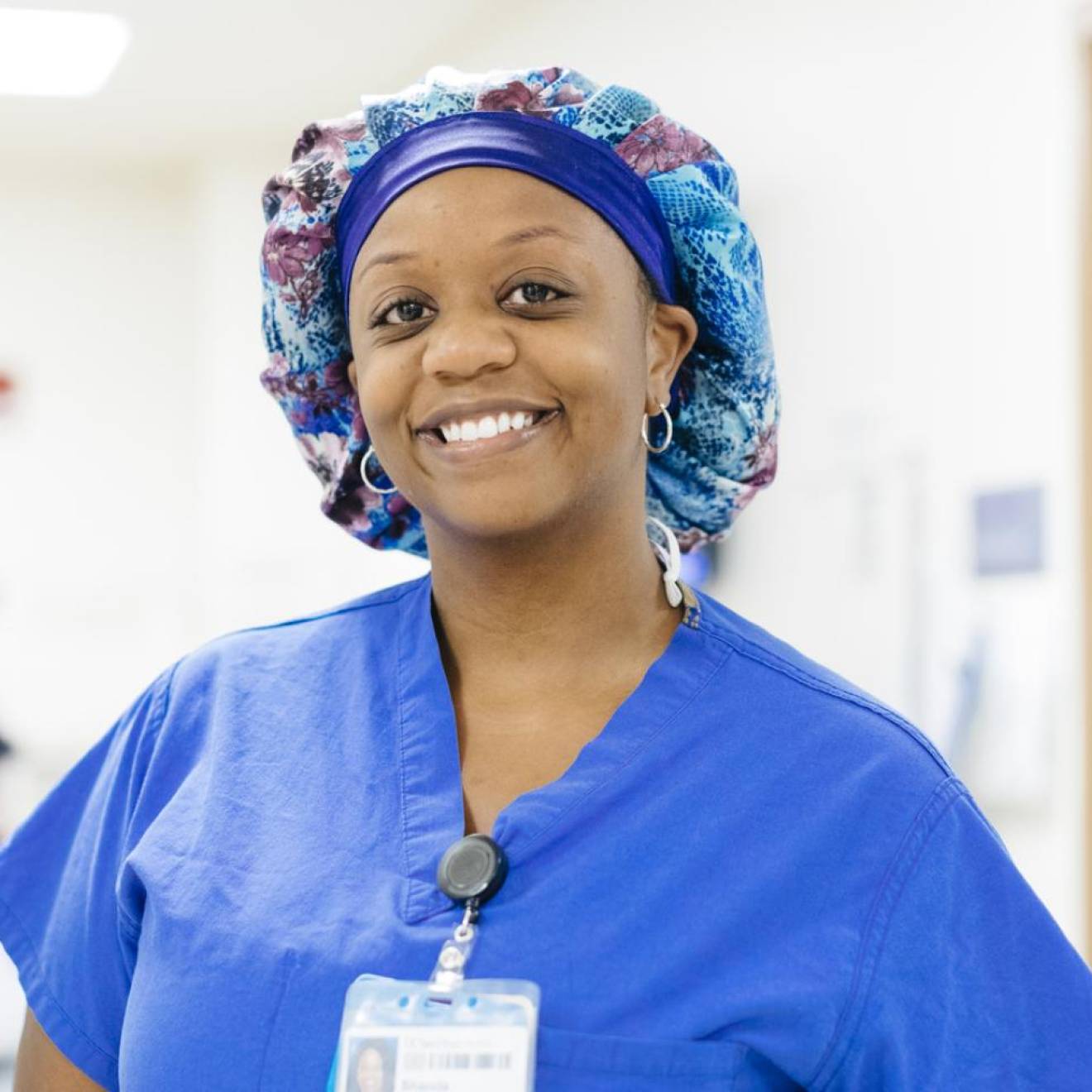 A nurse in scrubs and a hairnet smiles