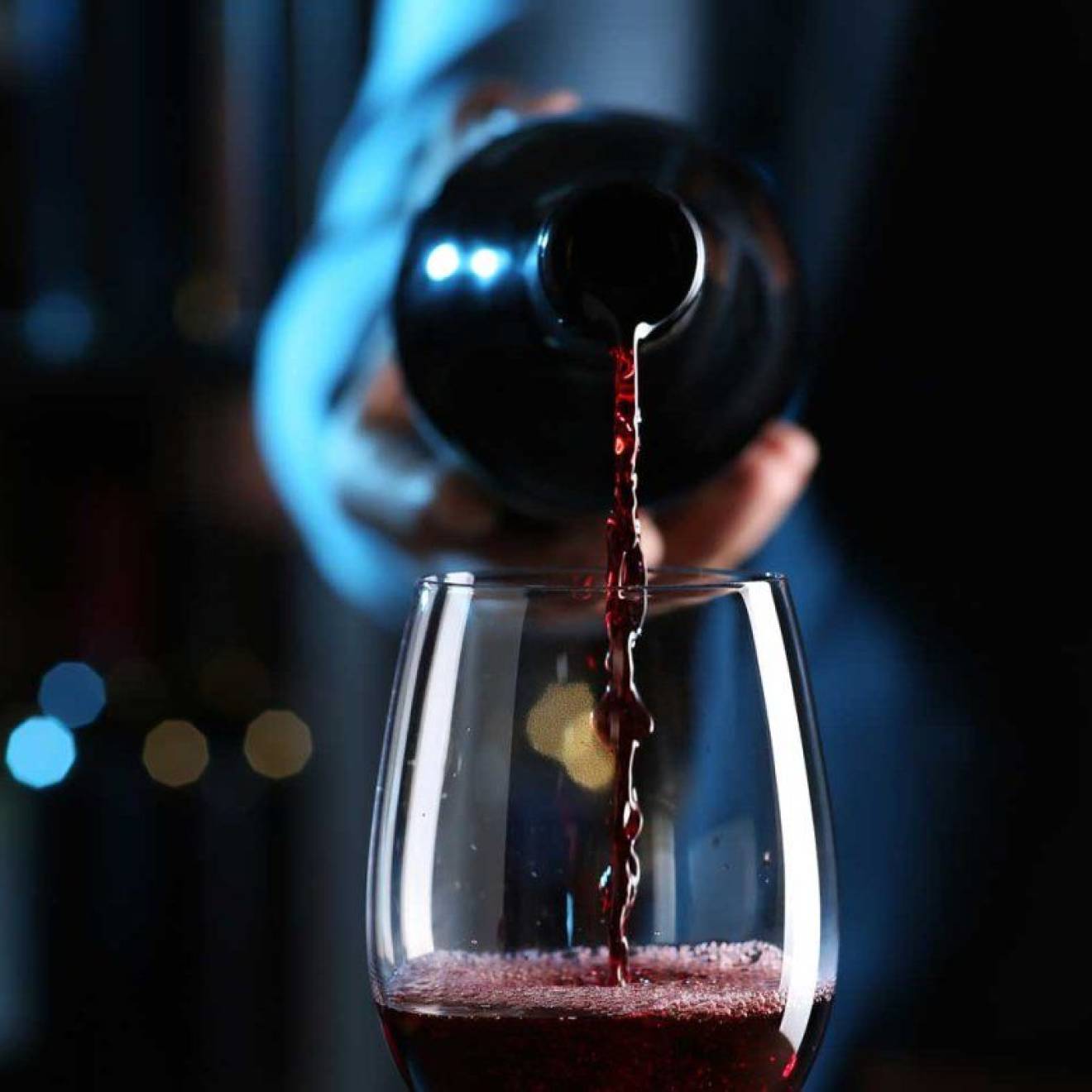 A hand pours a bottle of red wine into a wine glass, centered